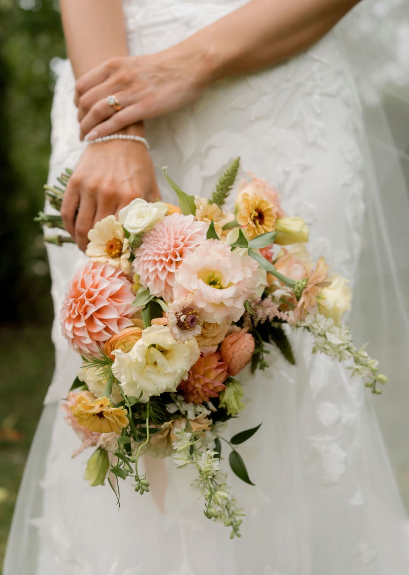 Close-up of a bride holding a hand-tied bouquet of peach dahlias, lisianthus, zinnias and ranunculus