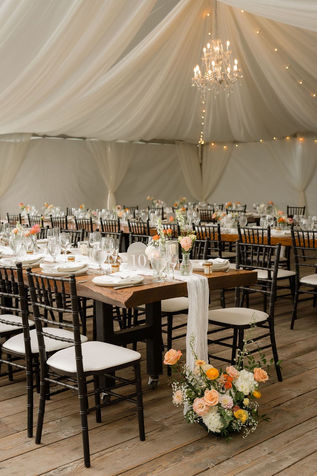 Reception tables under a white draped tent with a chandelier